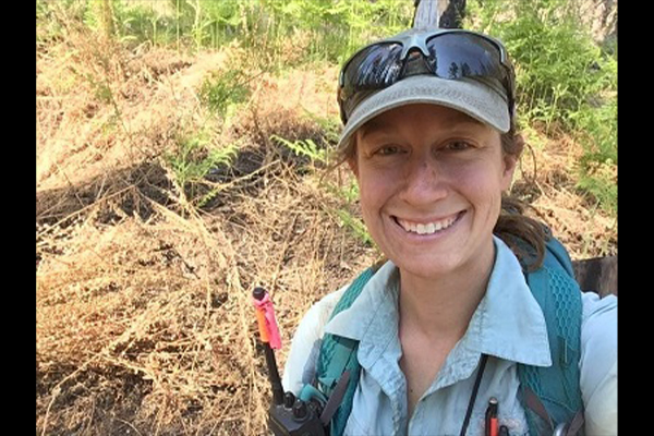 Dressed in field gear, a woman smiles at the camera.